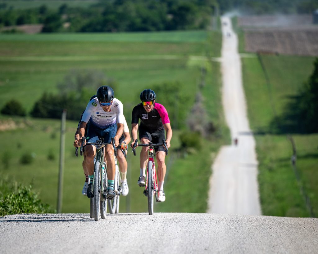 Three gravel racers climbing together on a rolling rural road